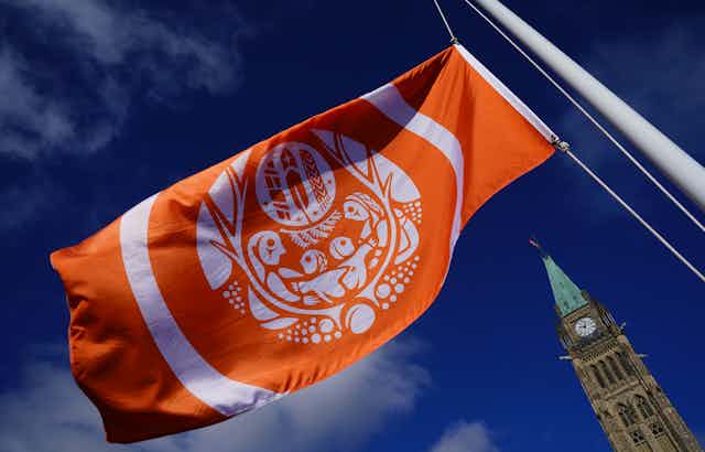 An orange flag with Indigenous artwork. The Peace Tower at parliament is seen in the bottom right of the photo.
