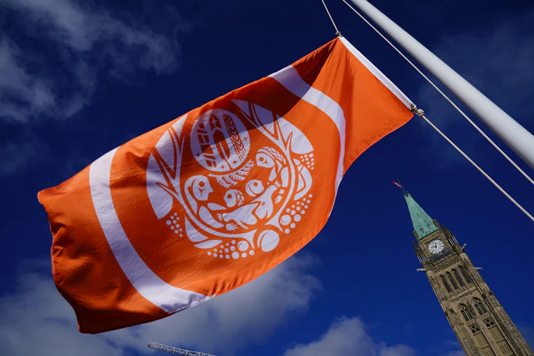 An orange flag with Indigenous artwork. The Peace Tower at parliament is seen in the bottom right of the photo.