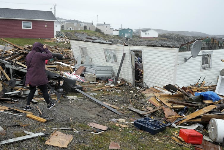 a woman walks up to the wreckage of a destroyed home
