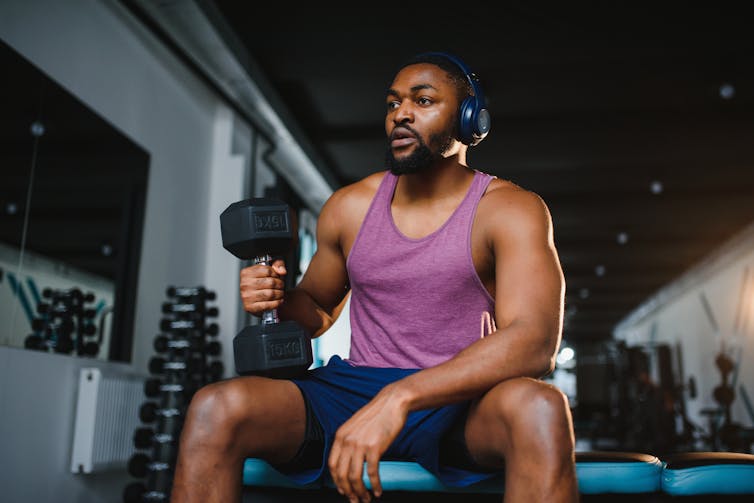 A man is seated on a bench in a gym, holding a weight.