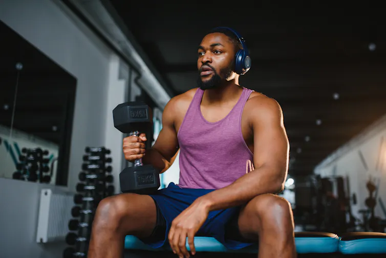 A man is seated on a bench in a gym, holding a weight.