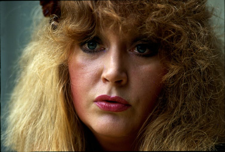 Portrait of woman with curly blond hair and tears welling in her eyes.
