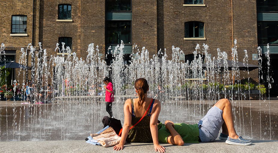 A couple sits beside a fountain trying to cool off the heat.