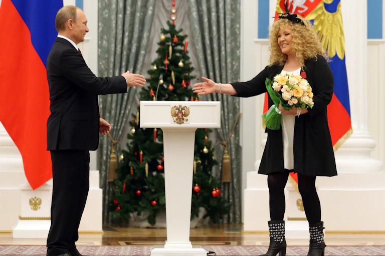 Man in suit about to shake hands with woman holding bouquet of flowers.