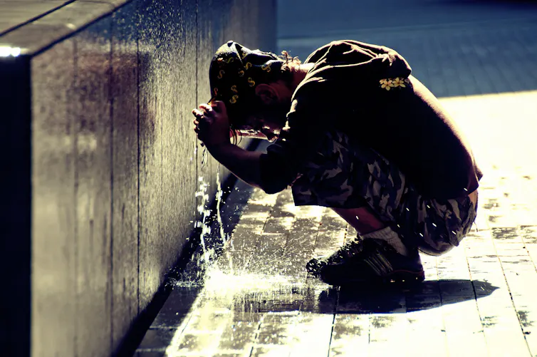 A man puts on a drenched cap to cool off