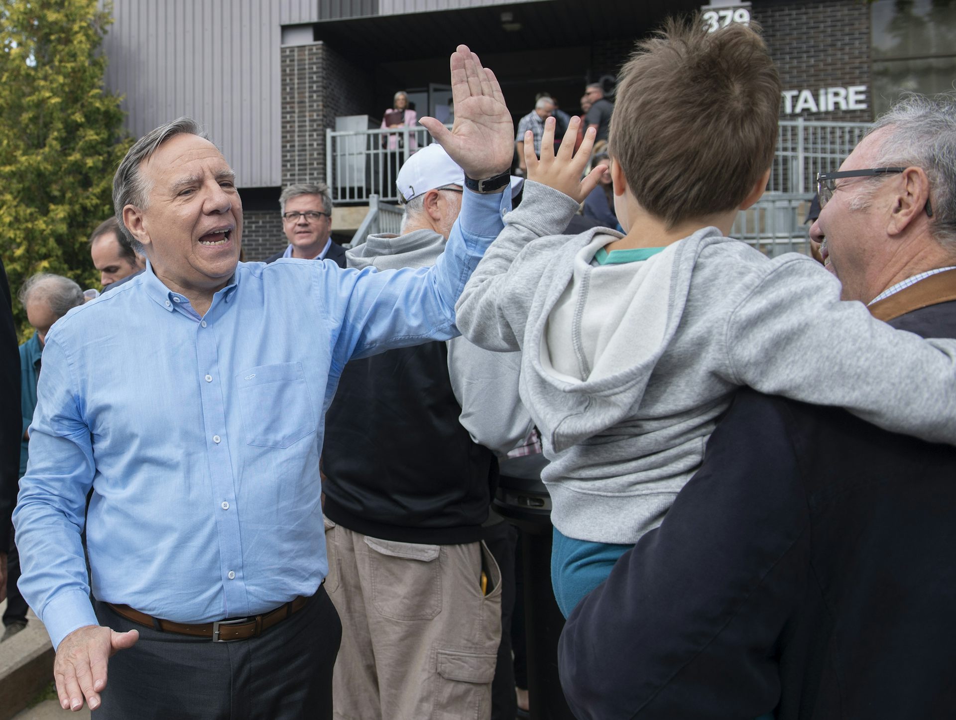 A man in a blue shirt high-fives another man holding a child.