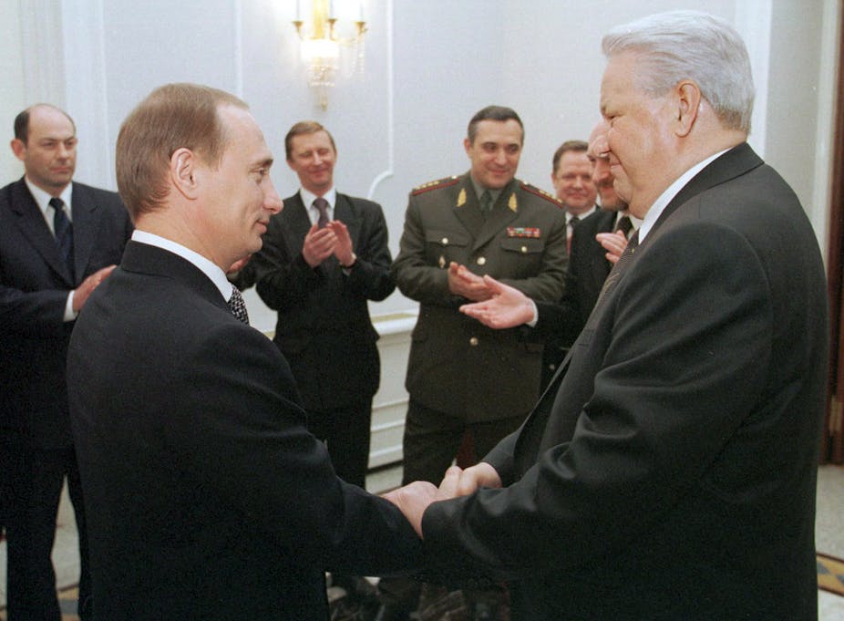 Vladimir Putin shakes hands with Boris Yeltsin as ministers applaud.