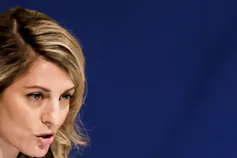 A blonde woman is seen in partial profile as she speaks.