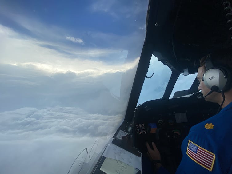 A pilot at the wheel, through the window of which a storm can be seen