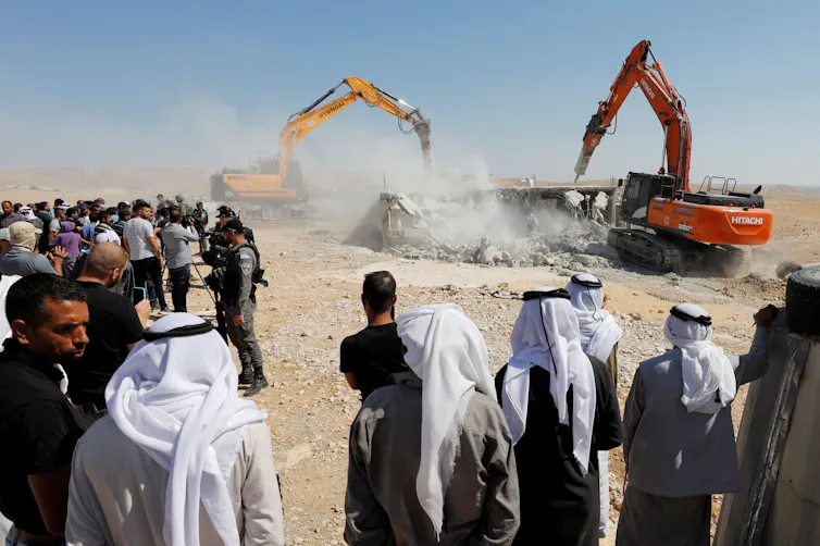 People watch as a house is destroyed by two mobile diggers