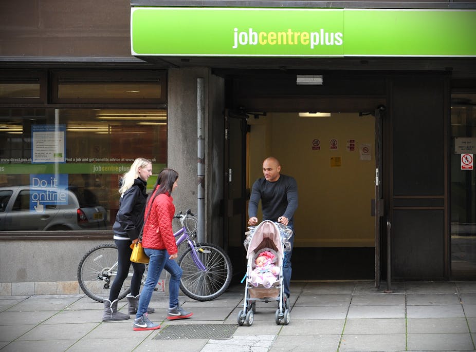 A man pushing a baby in a buggy, walking out of a jobcentre plus