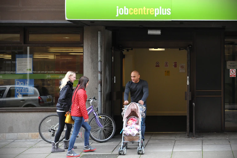 A man pushing a baby in a buggy, walking out of a jobcentre plus
