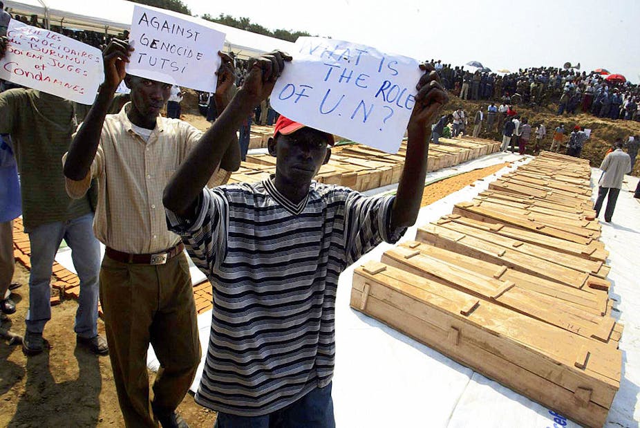 Men walking in front of tens of coffins holding up pieces of paper.