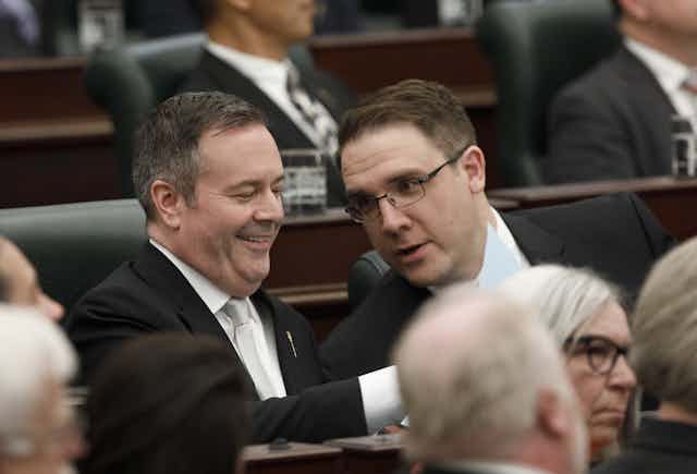 Two men in suits leaning toward each other talking and smiling