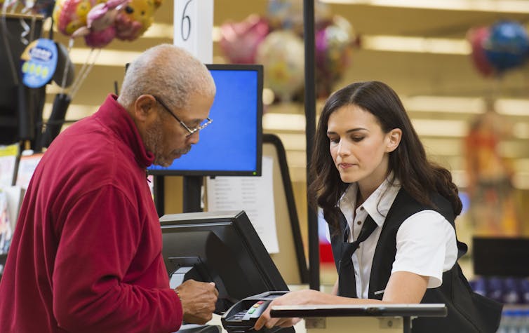 A man pays a clerk for items at a checkout counter in a store