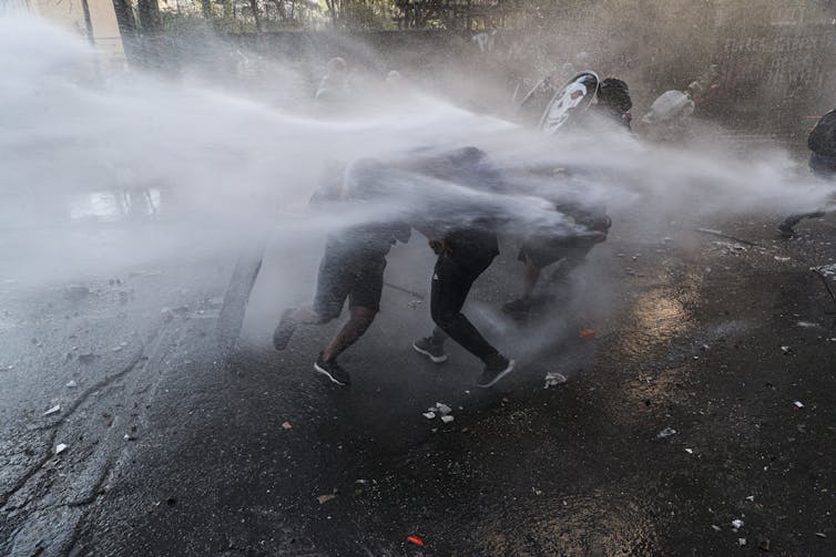 Police spray water at protesters. They are barely visible amid the jet sprays of water.