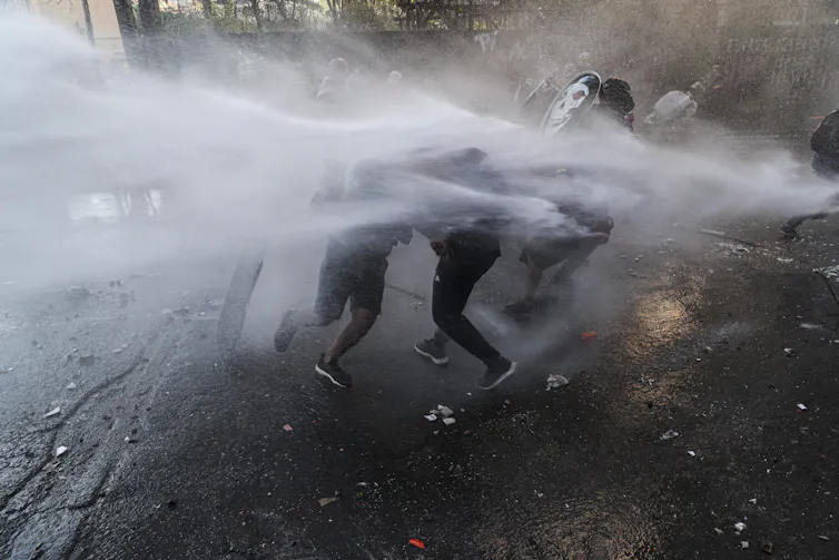 Police spray water at protesters. They are barely visible amid the jet sprays of water.