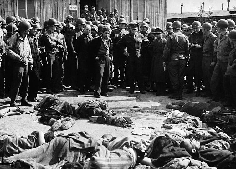 A black and white photo shows soldiers looking at bodies strewn in a courtyard.