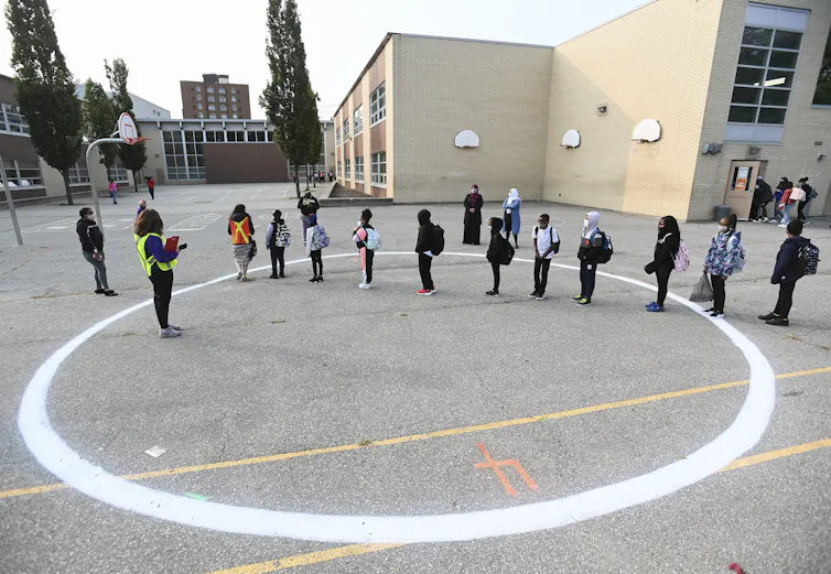 Children stand in a line in a schoolyard.