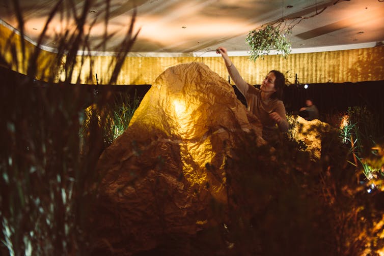 A woman stands over a tent made from brown paper.