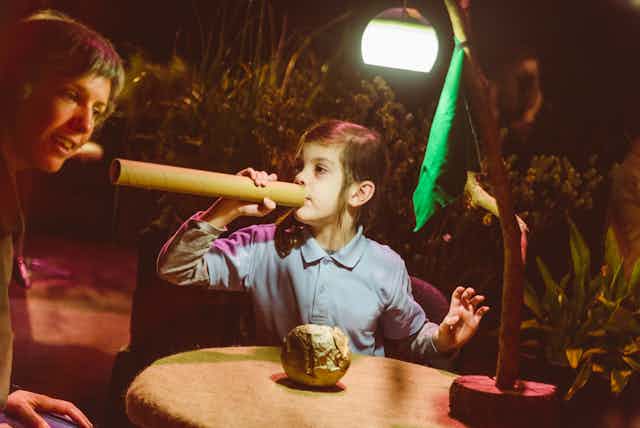 A young girl uses a cardboard tube as a trumpet.