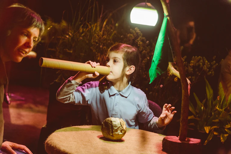 A young girl uses a cardboard tube as a trumpet.