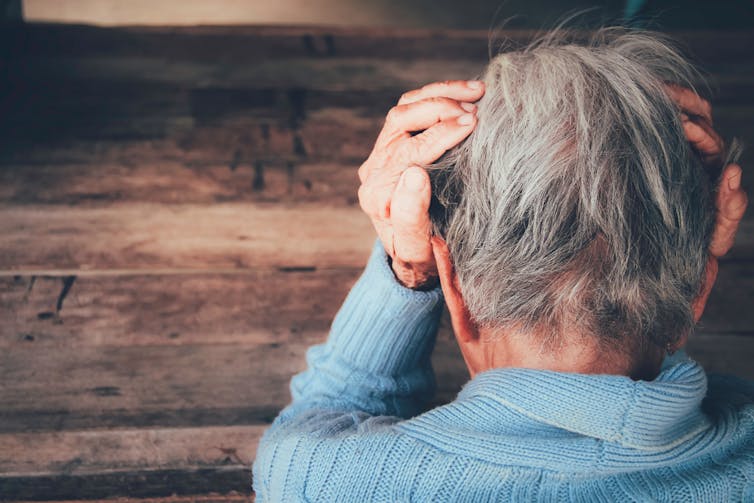 An older person puts their head in their hands.