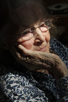 An older woman looks out the window.