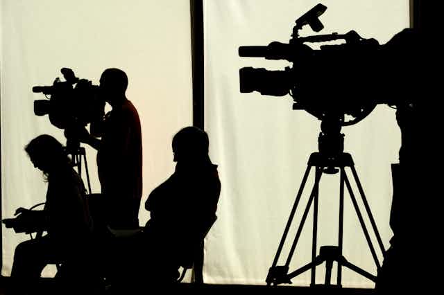 A group of journalists and camera people in silhouette.