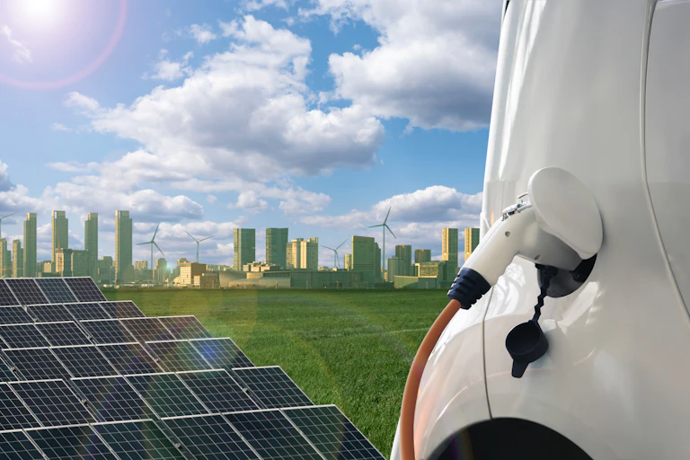 Rows of solar panels and an electric car charging in the foreground with a city skyline and wind turbines in the background.