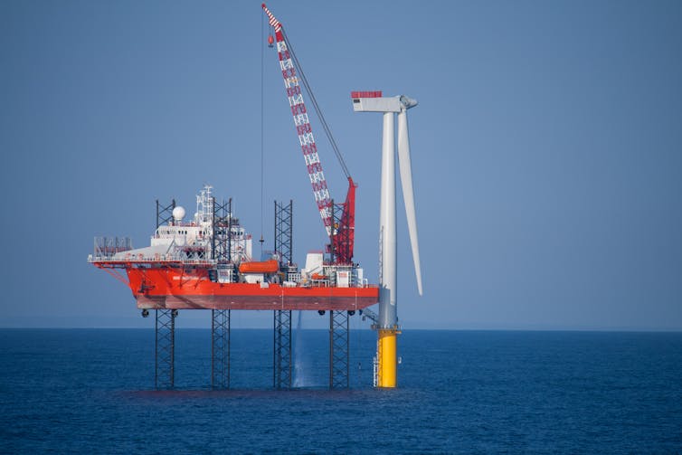 An offshore wind turbine being assembled by a crane on a ship.