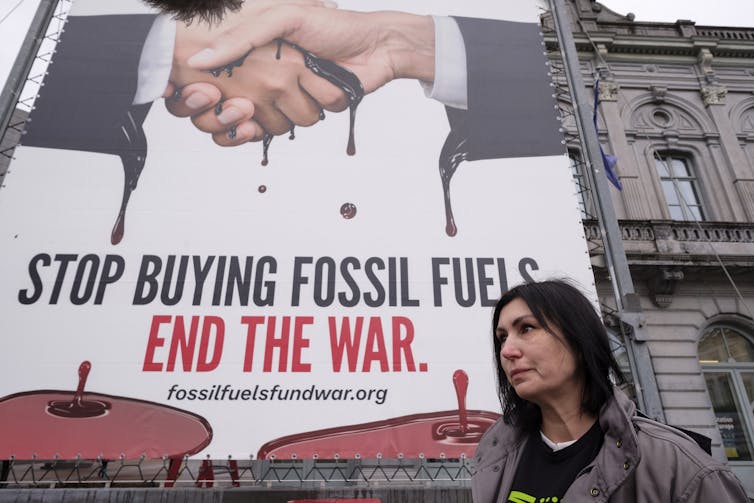 A woman walks past a billboard reading: Stop buying fossil fuels. End the war.