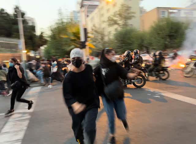 Deux femmes portant des masques s'enfuient devant des motocyclistes armés.