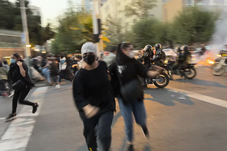Deux femmes portant des masques s'enfuient devant des motocyclistes armés.