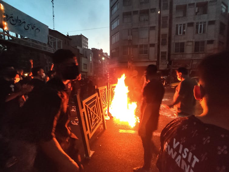 A fire burns in the street, surrounded by protesters