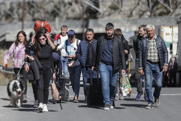 Russian men and women with their luggage walk along a road after passing through customs at the Georgia-Russia border, September 2022