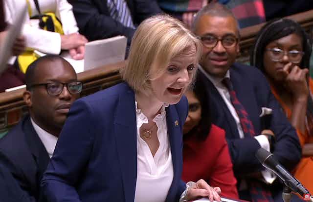 Liz Truss speaks into the microphone during PMQs, with Kwasi Kwarteng and other front benchers seated behind her.