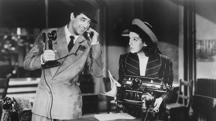 A man talks on the phone while looking at a woman, in a black and white film.