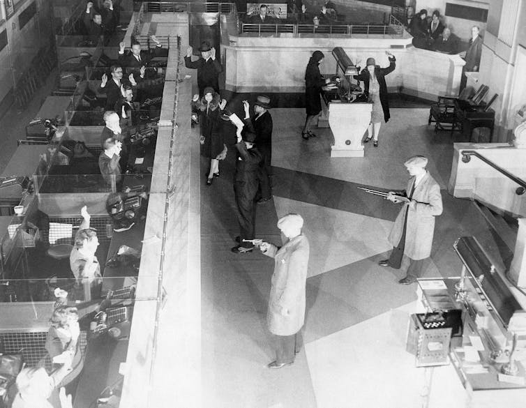 several men with guns point them at bank tellers in black and white photo