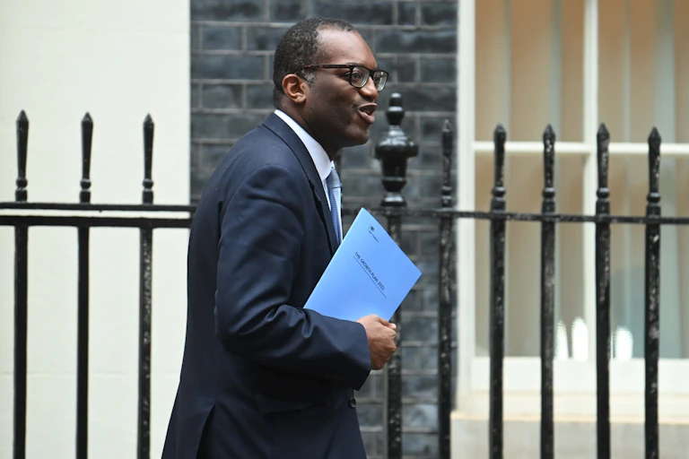 Kwasi Kwarteng walks past railings holding blue document