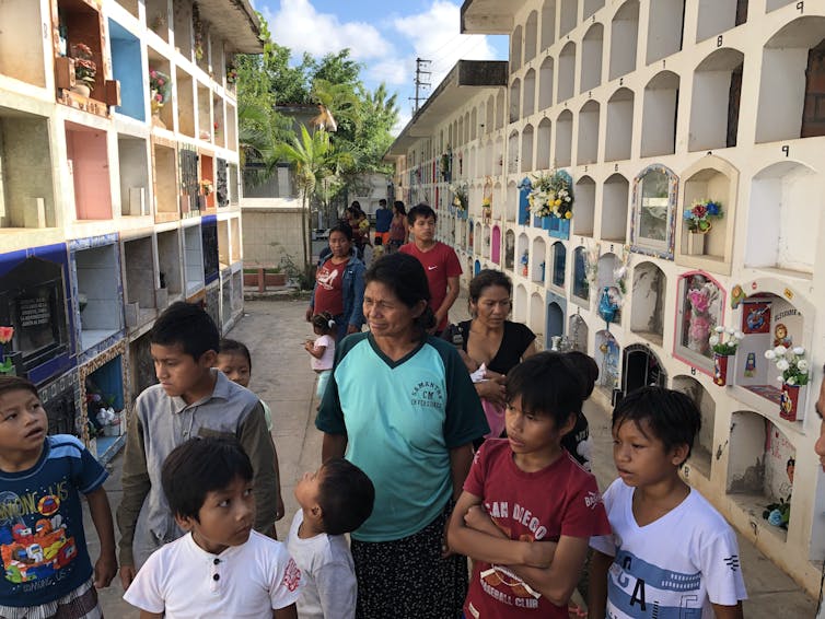 Un grupo de niños y adultos caminan frente a las bóvedas de un cementerio.