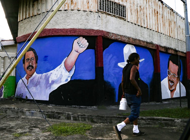 A woman walks by a mural of a man holding his fist in the air
