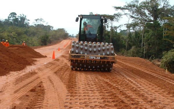 A worker aboard a Caterpillar road roller works on a road.
