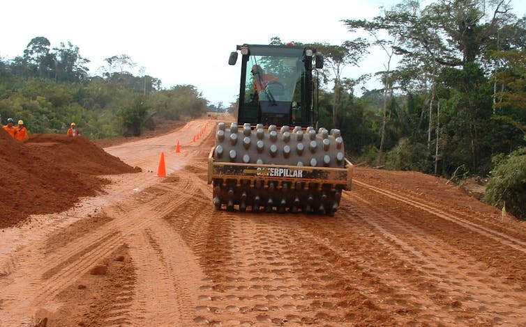 A worker aboard a Caterpillar road roller works on a road.