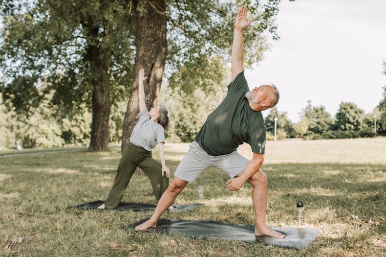 An older couple do yoga in the park.
