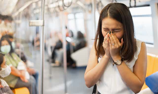 Woman on a train sneezes into her hand