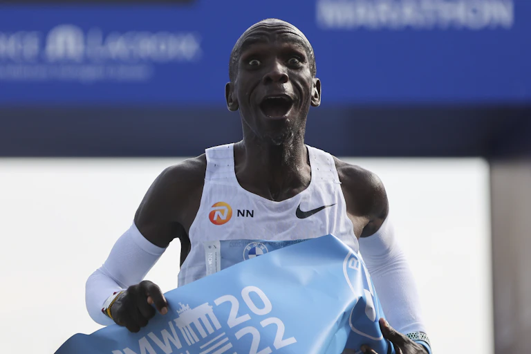 A joyful bald man running towards the camera with a large blue ribbon draped across him