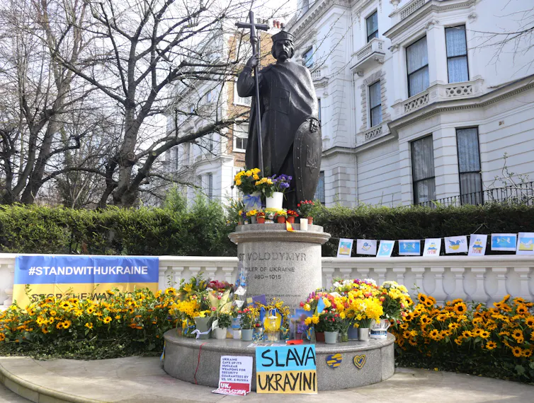 Flowers, drawings and notes around a statue in a city centre.