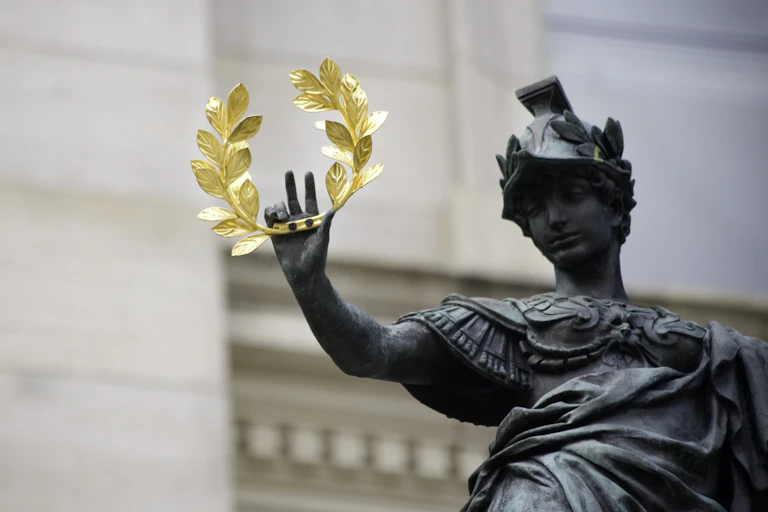 bronze statue of ancient soldier holding out gold laurel crown