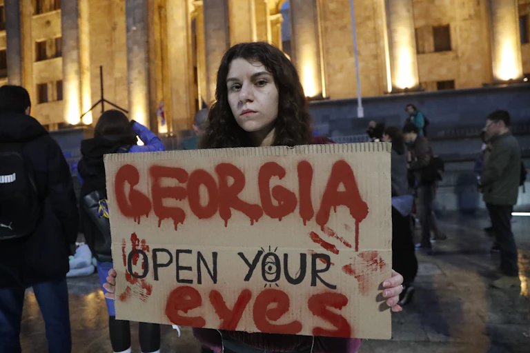 A Georgian woman holds up a signs saying: Georgia open your eyes